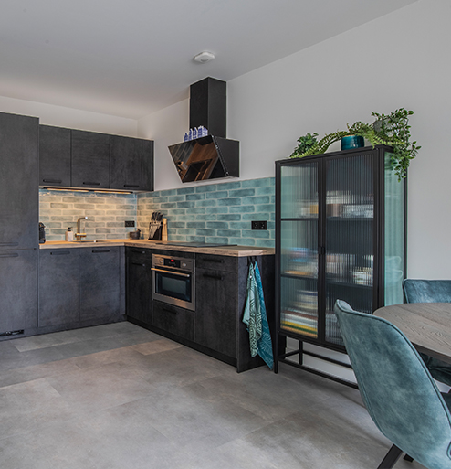 Open keuken met donkere kasten, groene tegelwand en stalen taatsdeur