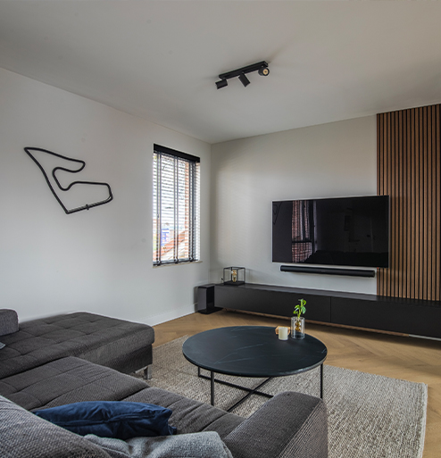 Strakke woonkamer met houten wandpanelen, wandmeubel en grote televisie